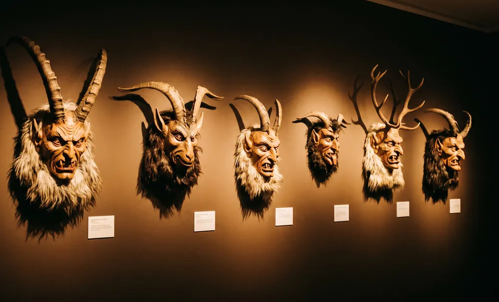 Sechs handgeschnitzte Krampusmasken nebeneinander an einer Wand im Ausstellungsraum